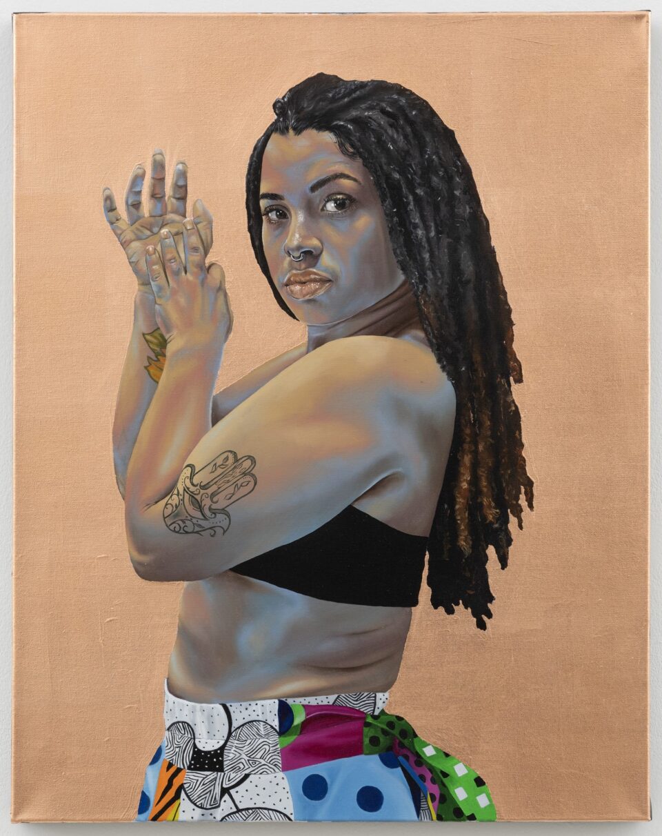 a portrait of a Black woman's torso, standing sideways and facing the viewer with her hands up in front of her face, showing a tattoo on her arm