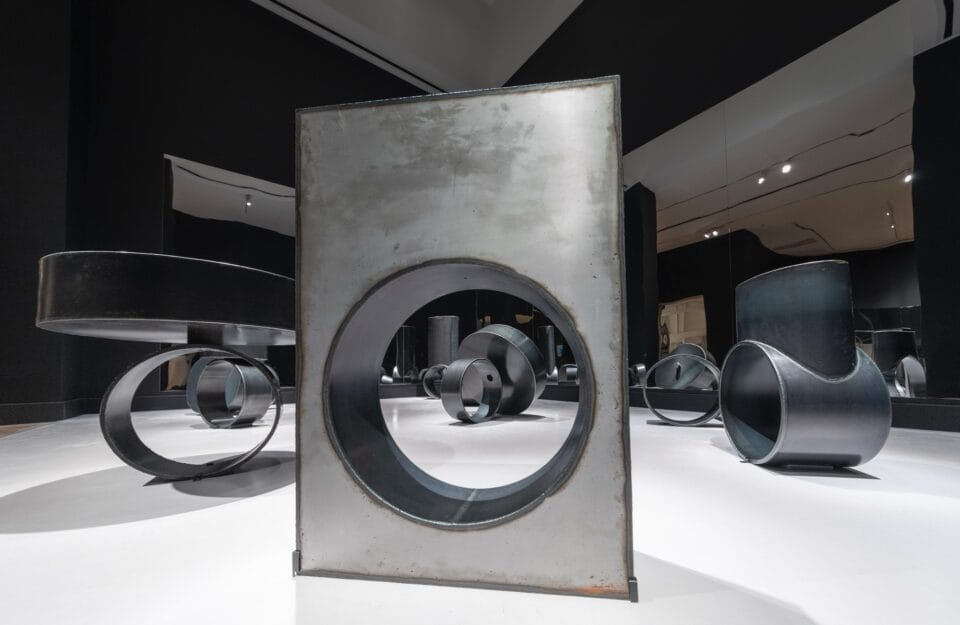 large metal sculptures resembling avant garde rings, installed in a black-painted museum gallery