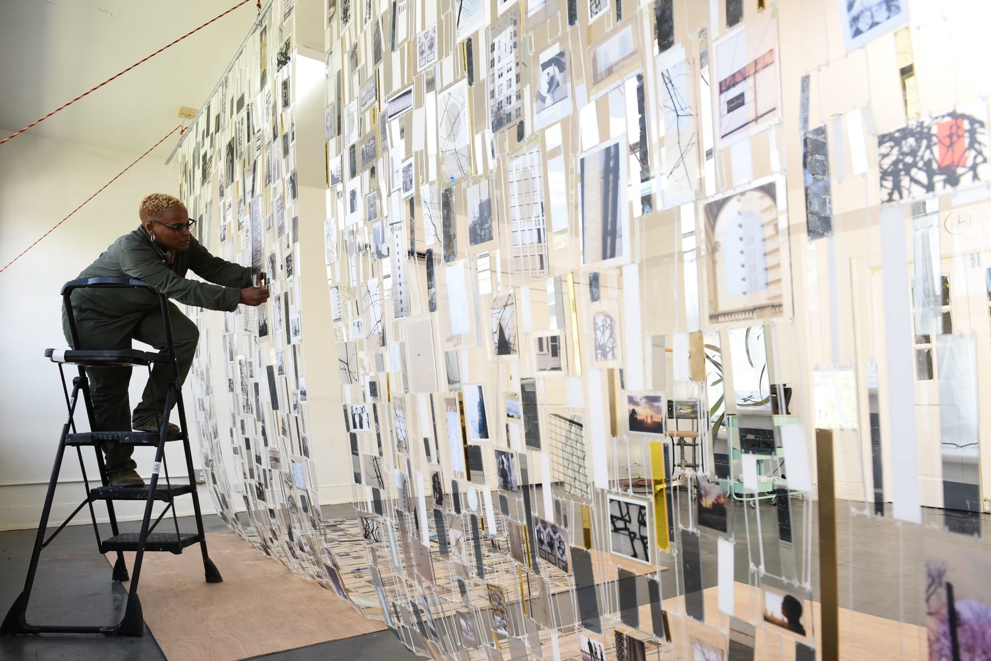 artist Lillian Blades standing on a step stool and working on a suspended mixed-media tapestry installation