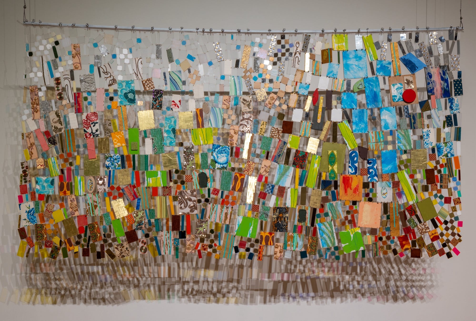 a colorful, suspended mixed-media tapestry installation, casting shadows on the wall