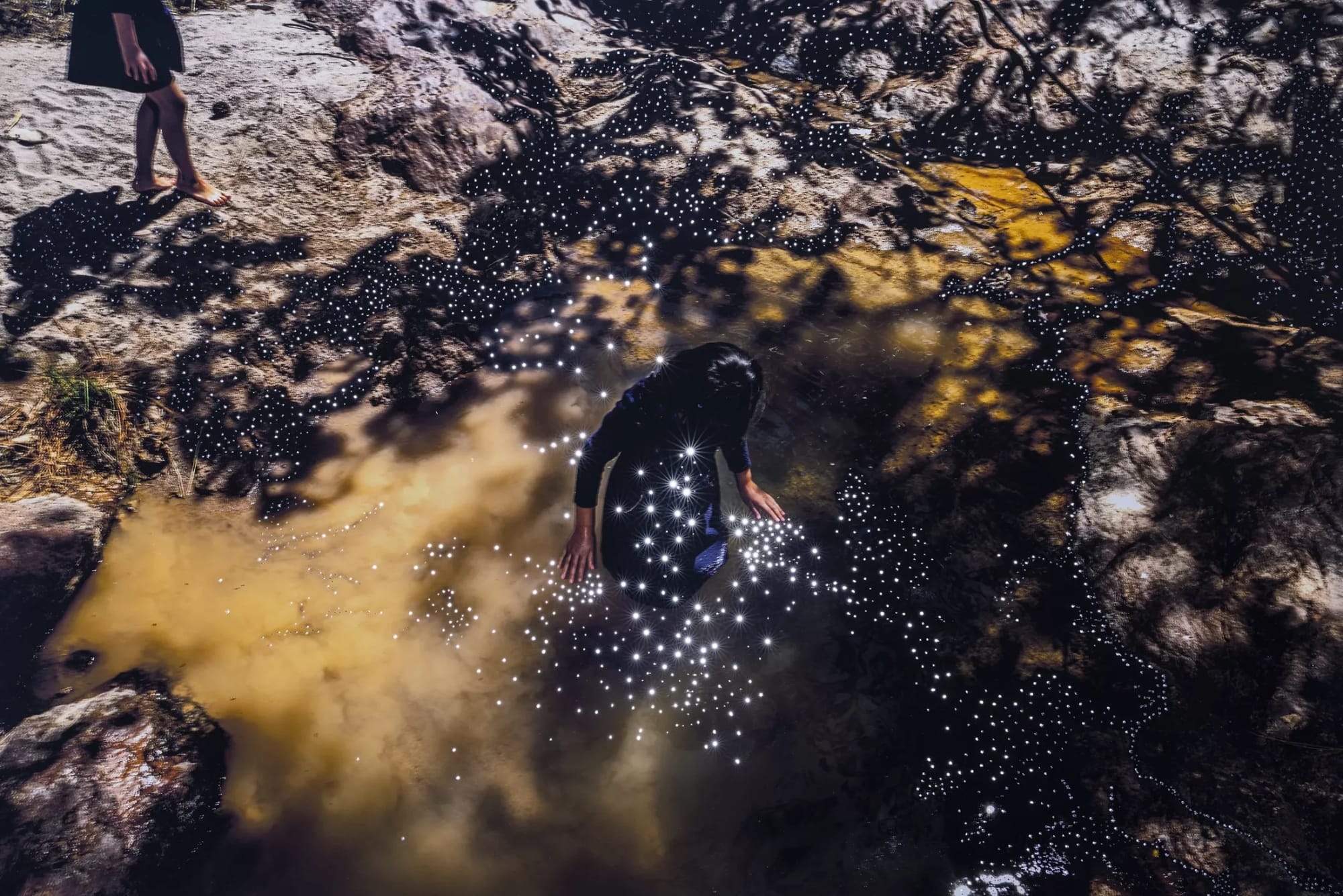 small holes pierce a dark photo of a woman wading in water