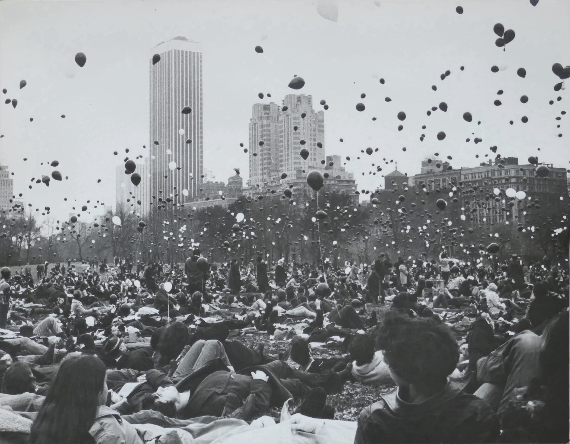 a black and white photo of balloons being released over a crowd of people on the ground