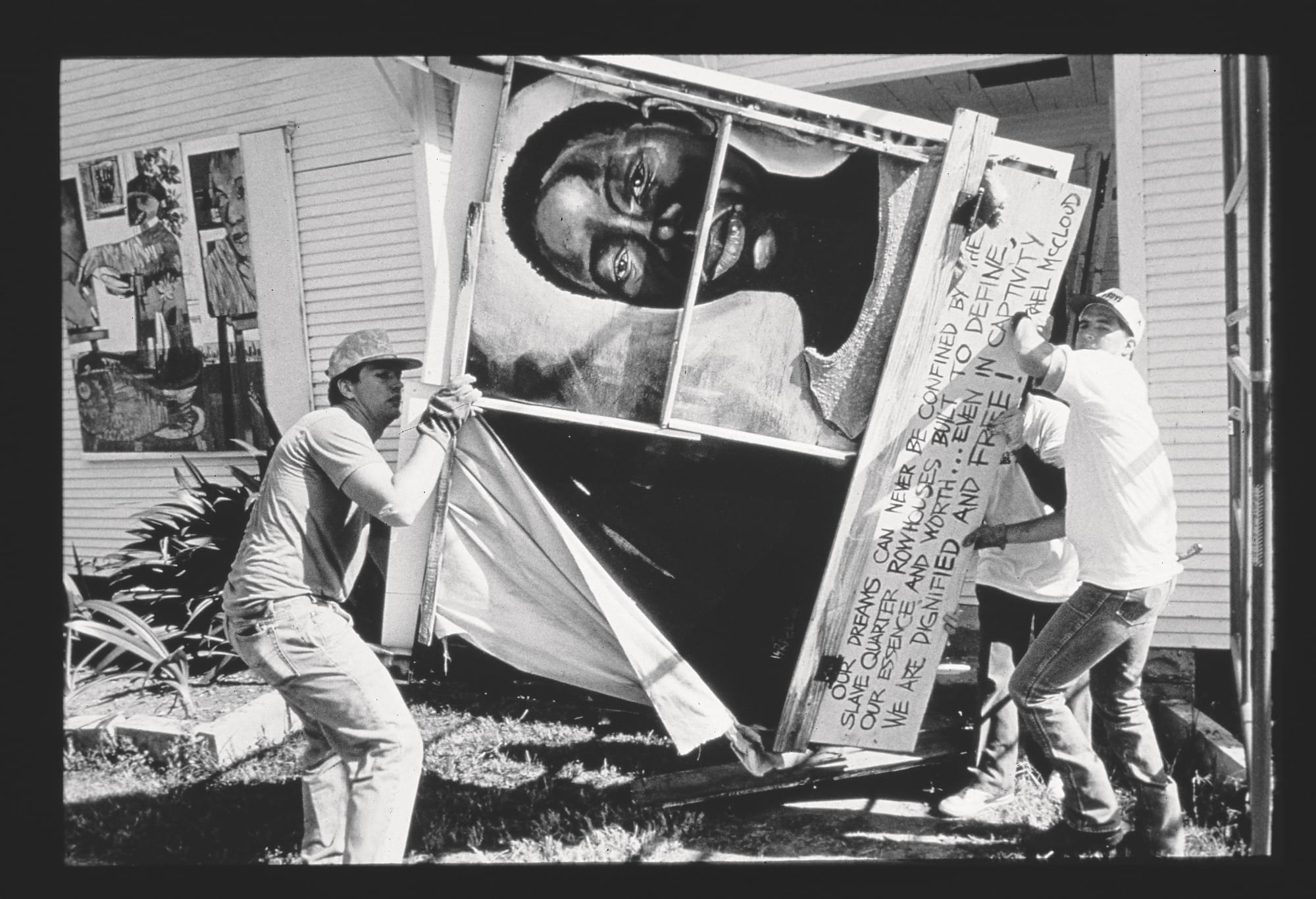 three men carry a large artwork with text and a portrait