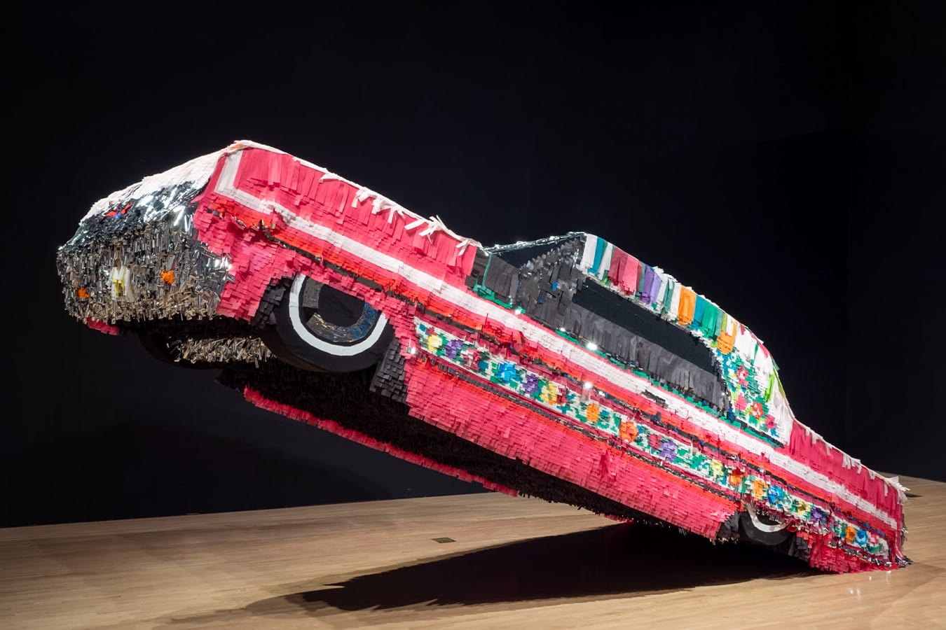 a sculpture by Justin Favela of a pink car with paper texture resembling a piñata