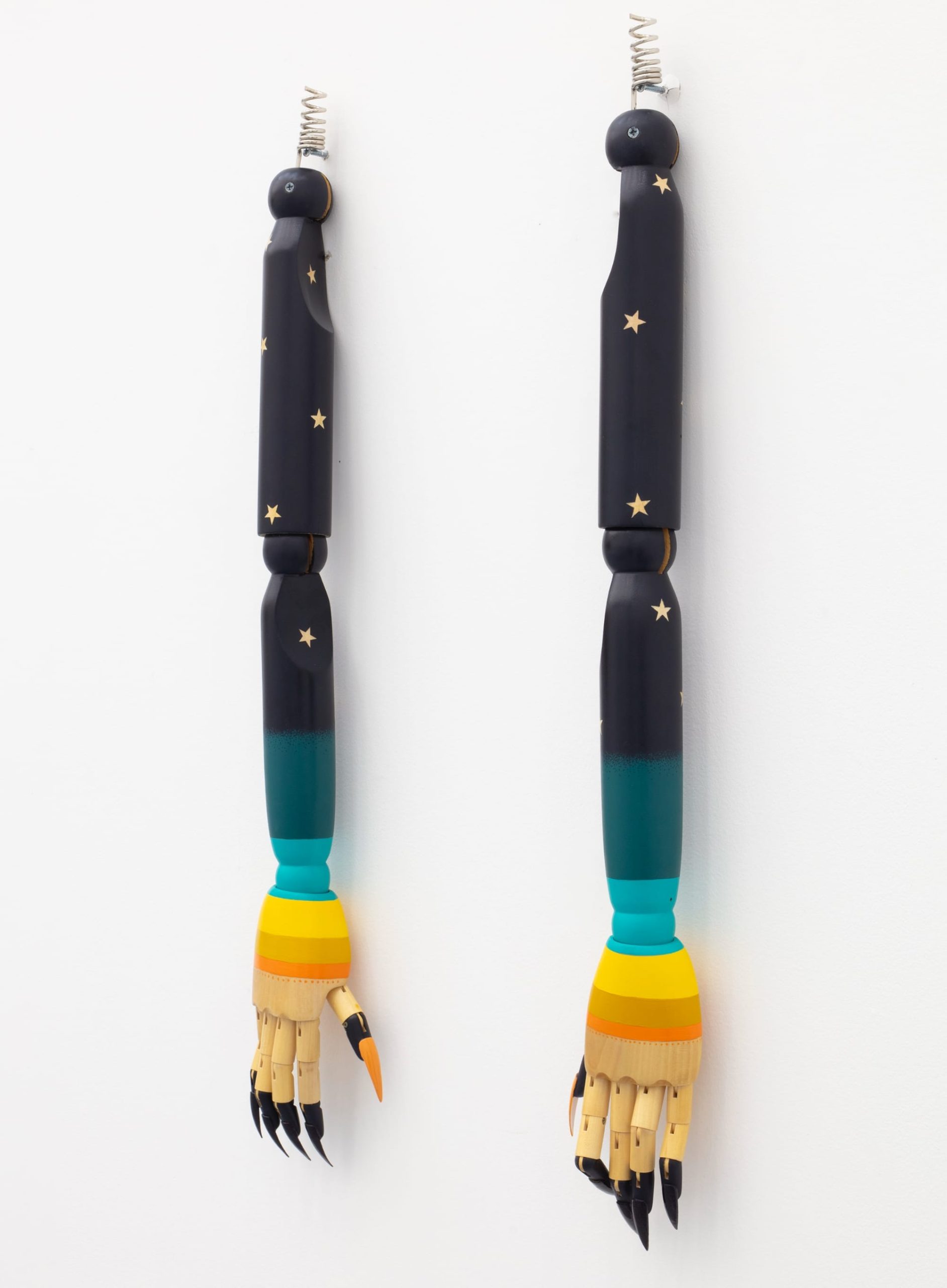 two wooden mannequin hands painted and hanging from long wooden arms on a wall