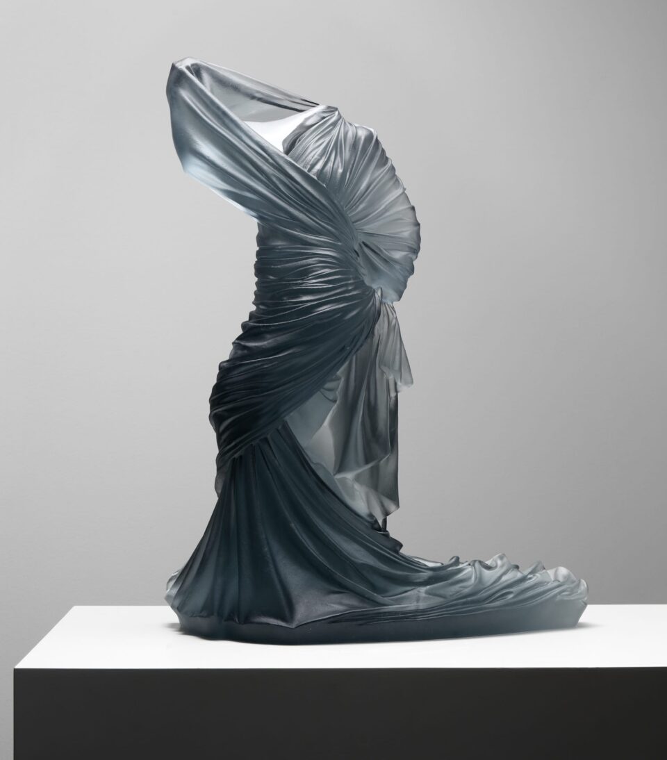 a cast glass sculpture of exaggerated drapery around a female figure, with no body present