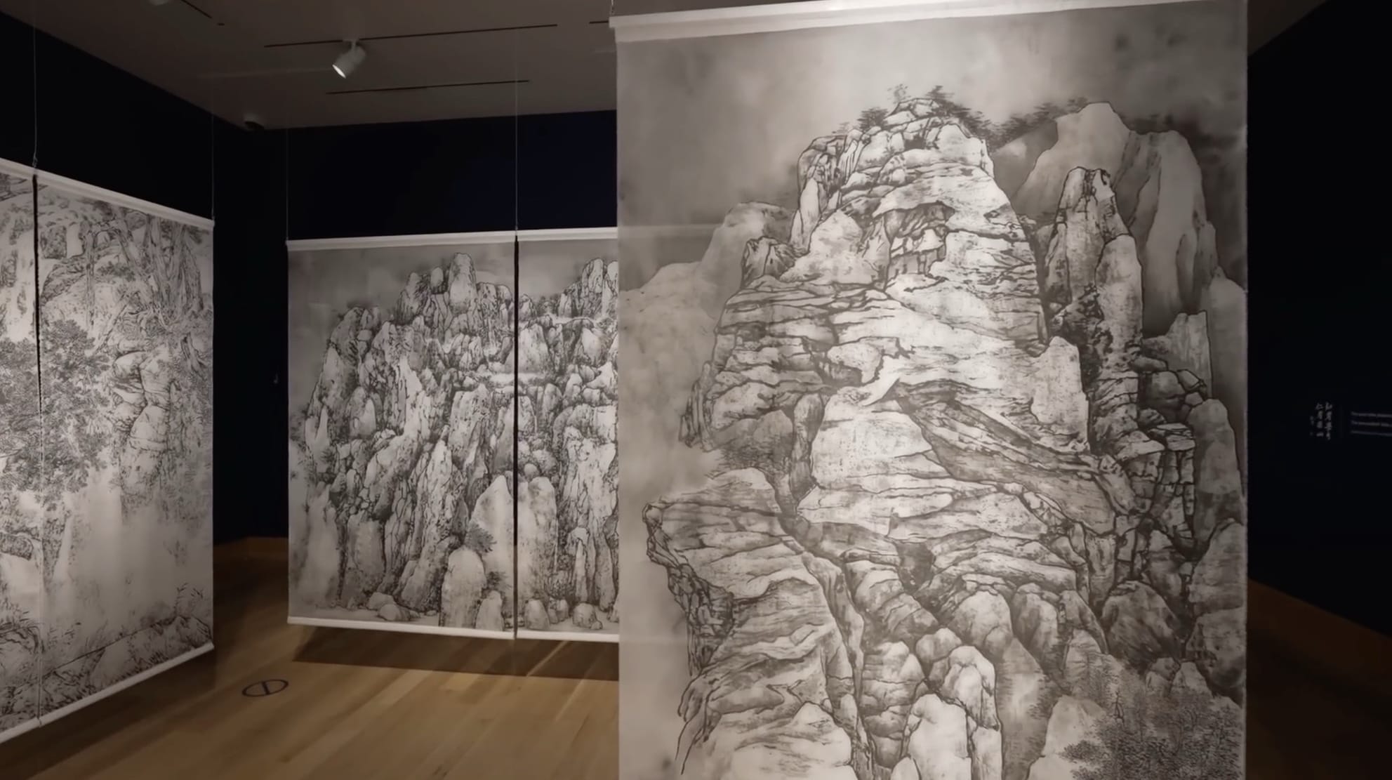 a still from a short documentary showing ink paintings on silk hanging in a gallery space