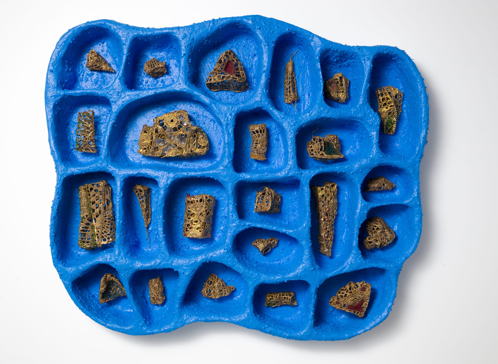 a blue cloud-like compartmented wall sculpture with niches for tiny crocheted objects