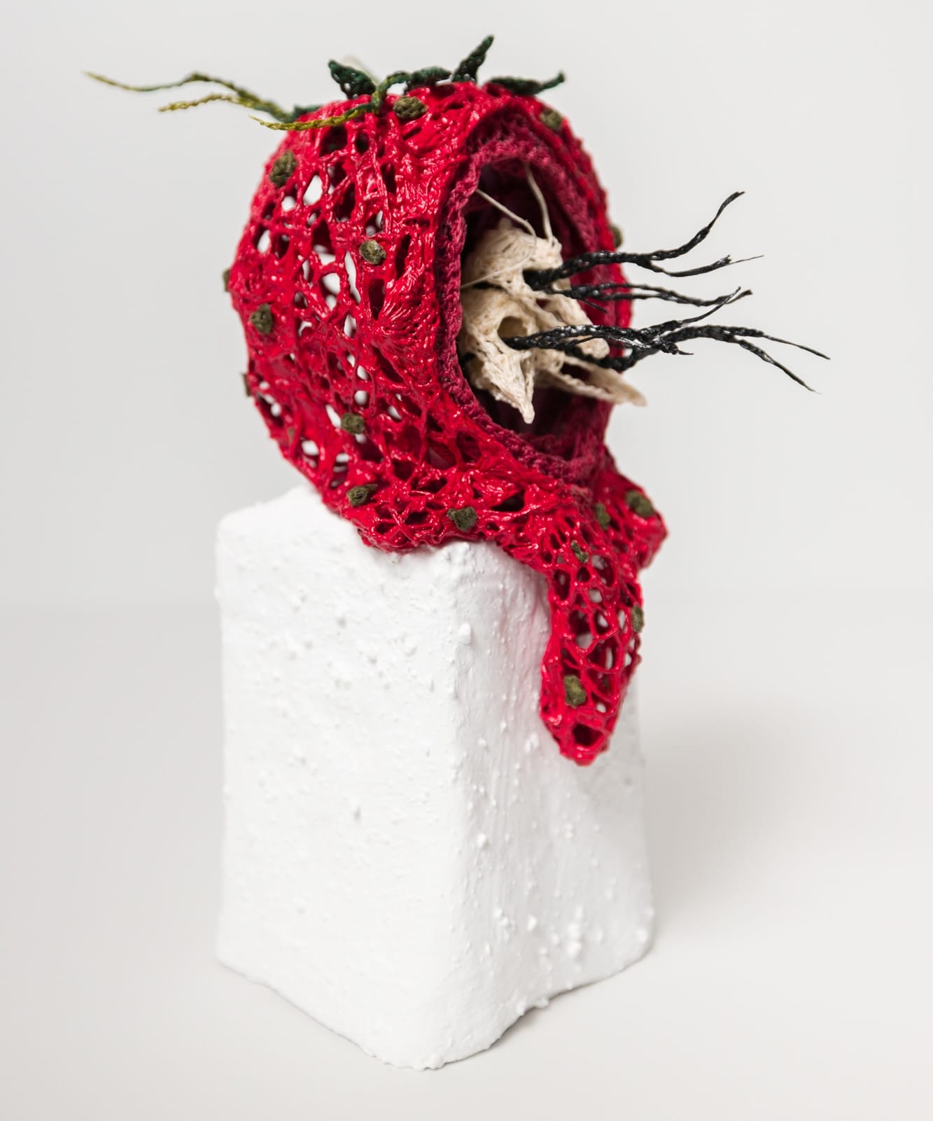 a crocheted sculpture of skeletal baby bird heads with black strands coming out of their eyes, surrounded by a red nest