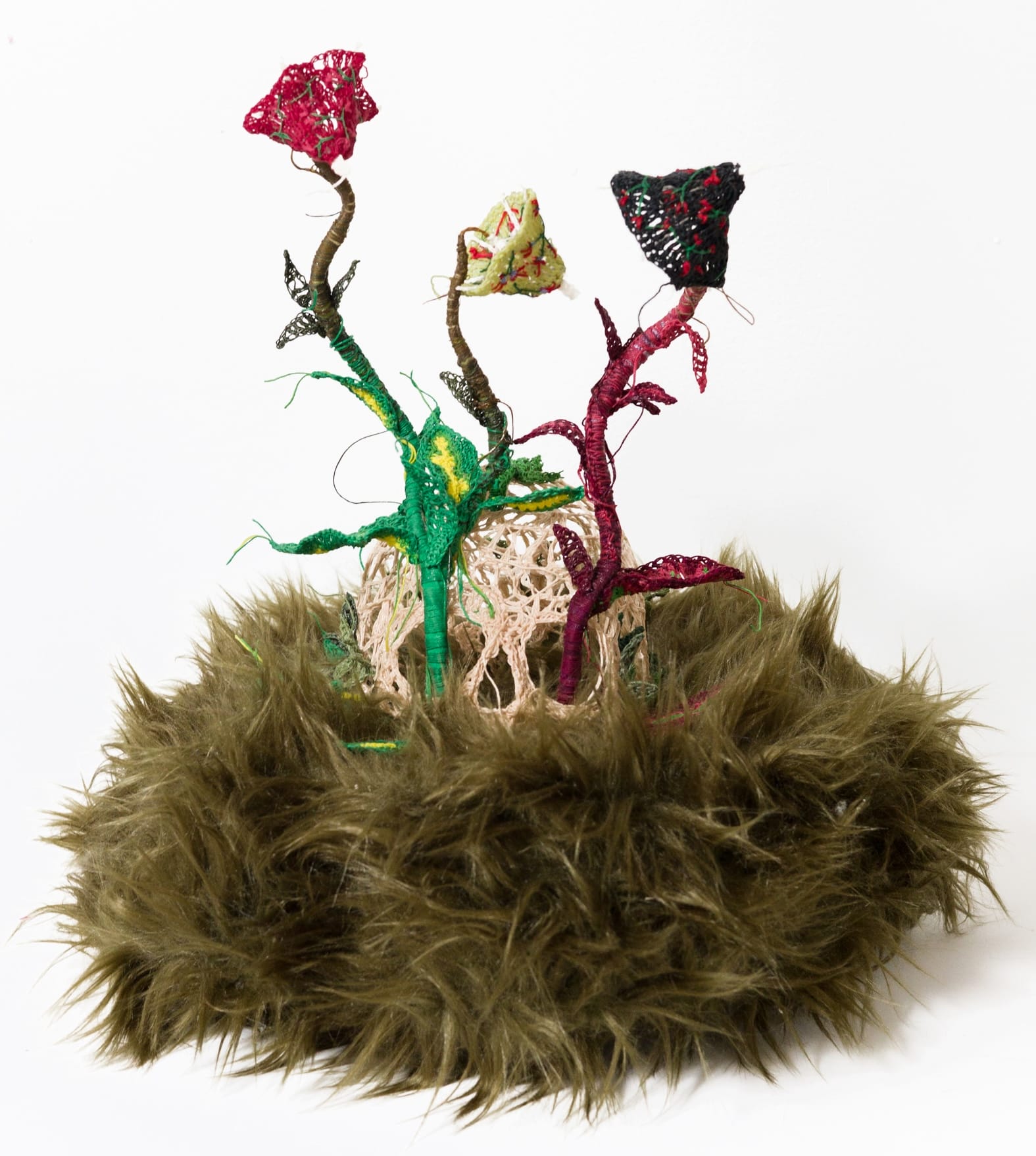 a textile sculpture featuring a crocheted human skill with plants growing out of the eyes