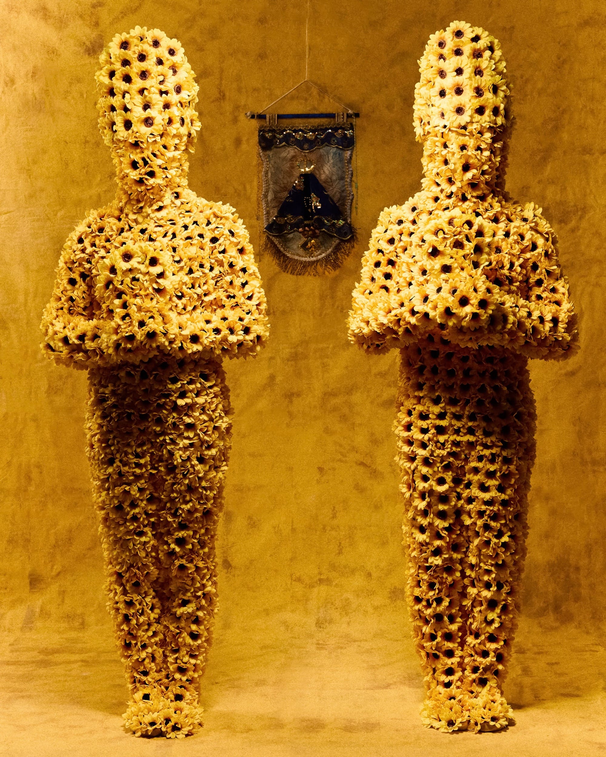 two figures in all-over costumes of fabric flowers, set against a yellow background