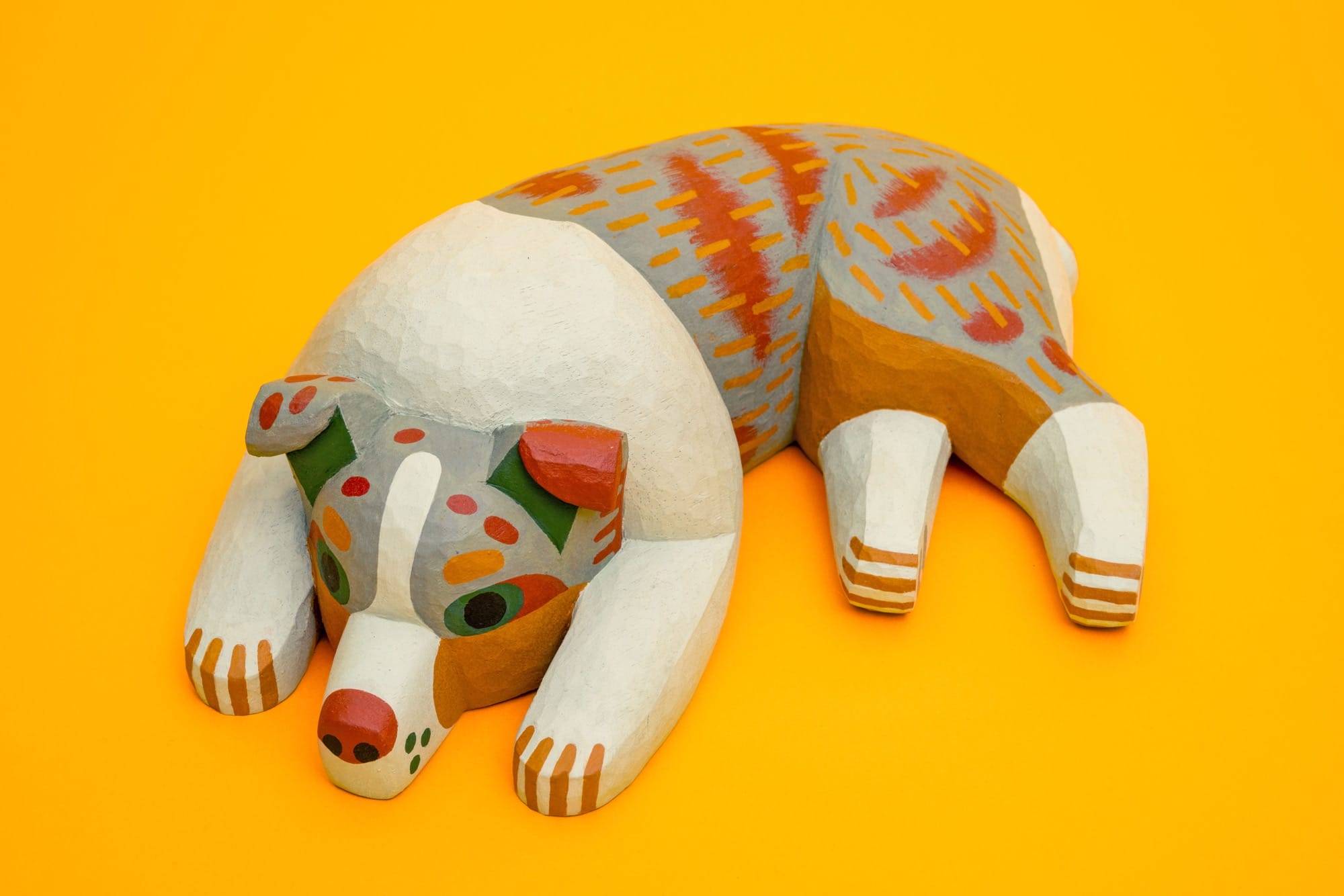a colorful, hand-carved wooden sculpture of a relaxing dog on a yellow background