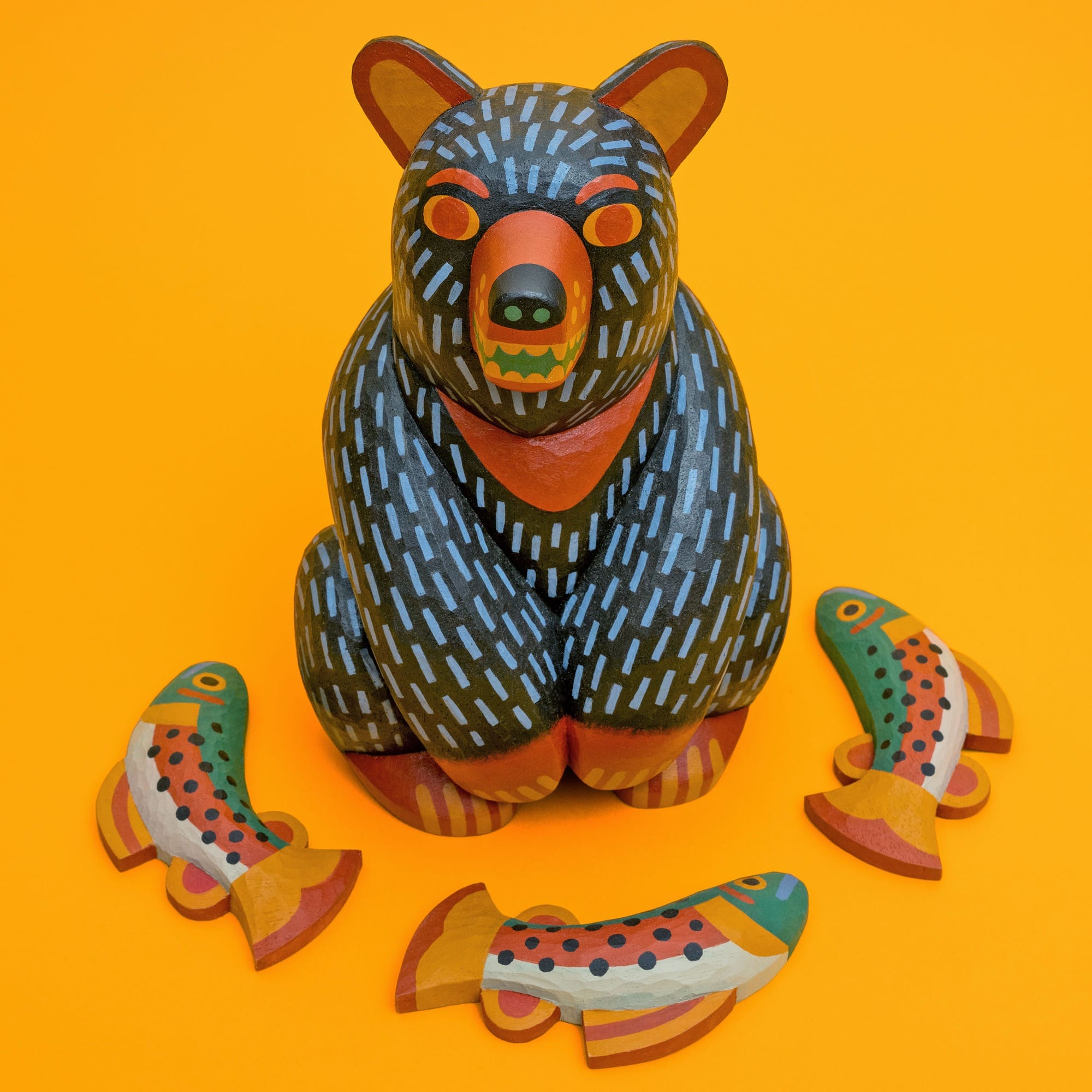 a colorful, hand-carved wooden sculpture of a bear on a yellow background, with three fish in front of it