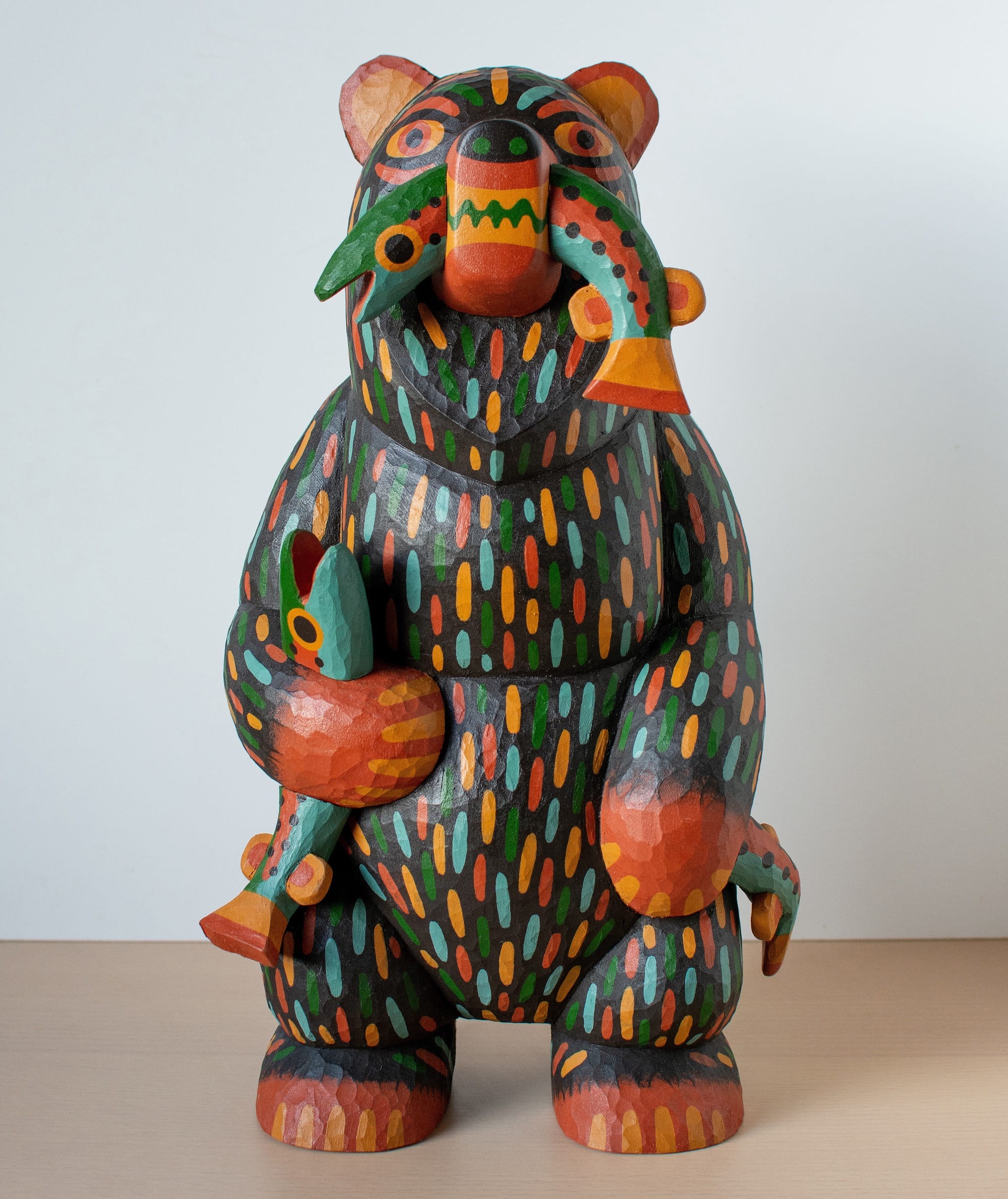 a colorful, hand-carved wooden sculpture of a bear with a fish in its mouth