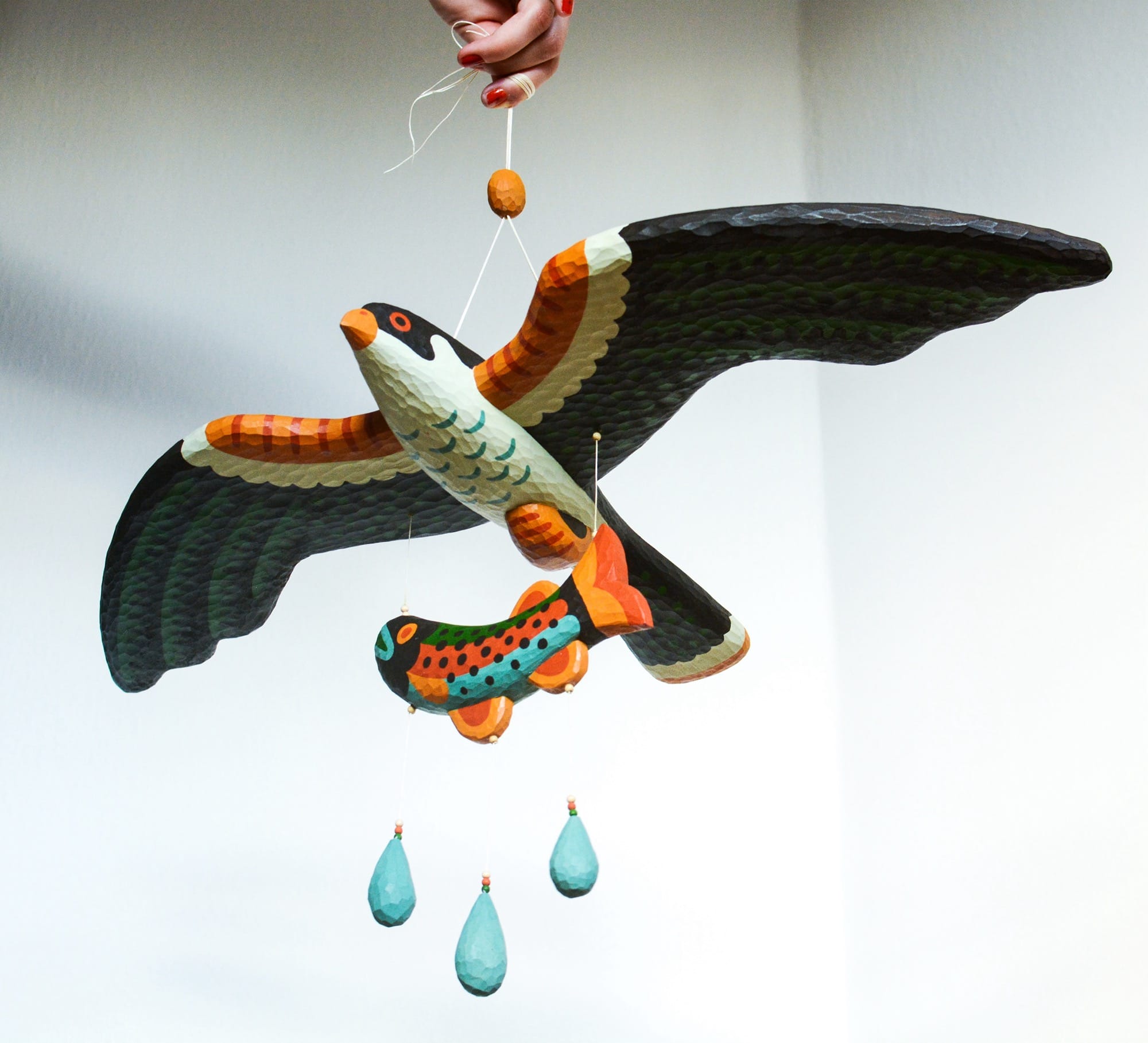 a colorful, hand-carved wooden sculpture of a bird of prey with a fish in its talons, suspended from a string